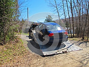 Blue car on a flatbed truck on a driveway