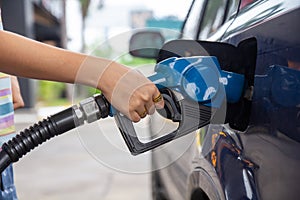 Blue car at gas station filled with fuel. Closeup woman hand pumping gasoline fuel in car at gas station