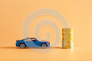 Blue car model and stack of golden coins against orange background. Concepts of saving money for a car, automobile insurance and