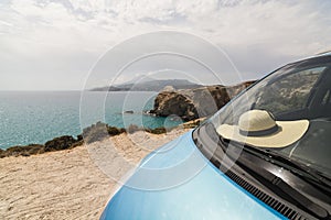 Blue car parked on sandy coast next to colourful rocks of Firiplaka beach on Milos island, Greece