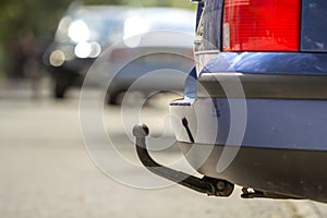 Blue car parked on sunny street, red stop lights, hook for dragging trailer, tow hitch or towbar.