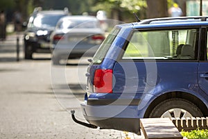 Blue car parked on sunny street, red stop lights, hook for dragging trailer, tow hitch or towbar.