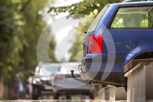 Blue car parked on sunny street, red stop lights, hook for dragging trailer, tow hitch or towbar.