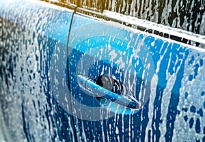 Blue car wash with white soap foam. Auto care business. Car cleaning and shining before waxing service. Vehicle cleaning service