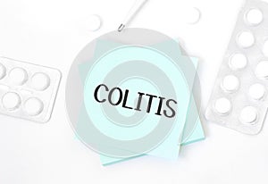 Blue card with text COLITIS on a table with a pills and pencil, medical concept, top view