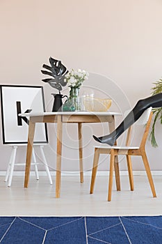 Blue carpet and model`s leg in dining room interior with chair at wooden table with leaf. Real photo