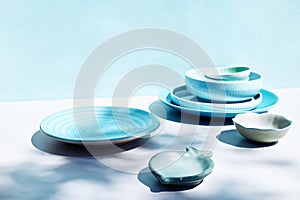 Blue ceramic bowls and plates on white and blue background. Colorful ceramic empty dishes with hard shadows.