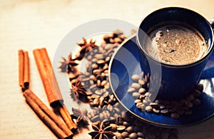 Blue ceramic cup with black coffee drink and coffee beans, cinnamon and star anise spices