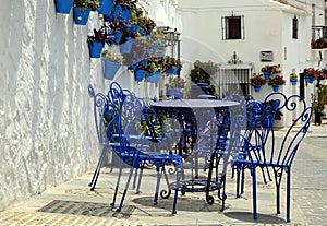 Blue chairs and tables, next to traditional blue plant pots with Geraniums, attached to a white-washed wall, Spain