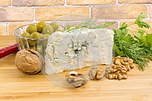 Blue cheese with blue-grey mold among walnuts, olives, greens