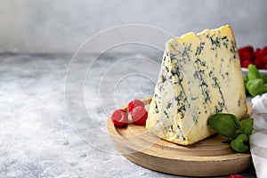 Blue cheese, dor blue or roquefort mold cheese slice on cutting board with basil leaves and rasberries, lifestyle food