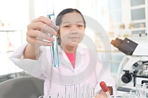 Blue chemical test tube in hand of young scientist schoolgirl wearing lab coat. Student girl child use lab equipment to do science