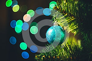 Blue Christmas ball on the spruce Christmas tree with multicolored bokeh round garland lights background