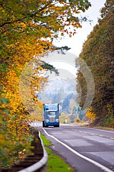 Blue classic modern semi truck on winding autumn road