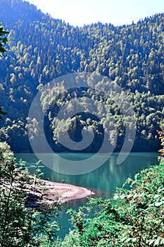 Blue clear emerald lake glowing in the sun near green trees high in Abkhazian mountains