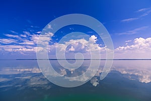 Blue clear sky with white clouds reflected in calm water of sea on Sunny day