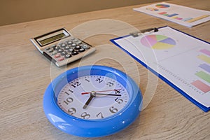 Blue Clock, calculator, pen, graphics on table. Businesses concept