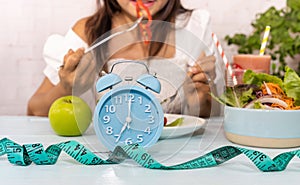 Blue clock for Intermittent fastin concept and woman eating salad background in the kitchen