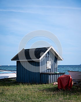 A blue closed wooden fishing hut next to some boats just by the beach in southern Sweden