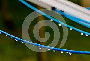 Blue clothing lines of a clothes spin with many raindrops at the string in front of a green background, after the rain. Retro way