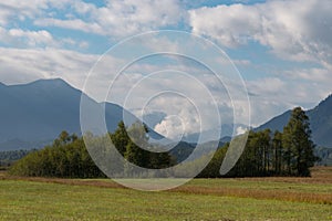 A blue cloudy sky above Bavarian mountains and trees in a cozy rural countryside.