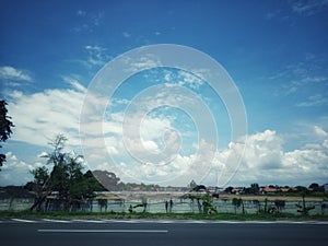 Blue cloudy sky with lake puddle water pond and urban housing below situated in highway sideway