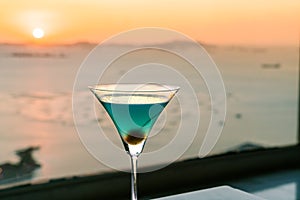 Blue cocktail with cherry on window view of sunset
