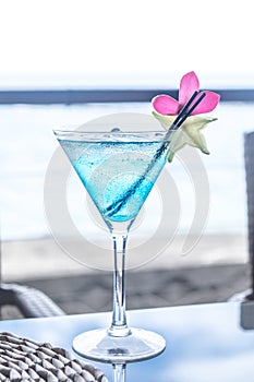 Blue cocktail in a martini glass with pink flower garnish and st