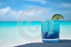 Blue cocktail on the white sand of a paradisiacal beach with the sea in the background. Copy space. Ai generative