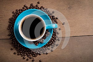 A blue coffee cup full of black coffee on a wood background with coffee beans