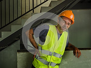 Blue collar job lifestyle. Portrait of tired and exhausted construction worker in helmet and vest at building site complaining of