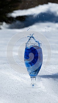 Blue color splashing out of a glass with egg on snow background