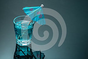 Blue colored cocktail drink with umbrella on black mirror background