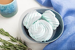 Blue colored homemade zephyr or marshmallow with cup of coffee on white wooden background. side view, selective focus