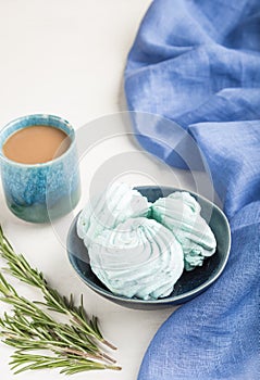 Blue colored homemade zephyr or marshmallow with cup of coffee on white wooden background. side view, selective focus