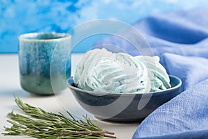 Blue colored homemade zephyr or marshmallow with cup of coffee on white wooden background. side view, selective focus