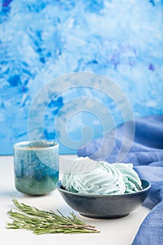 Blue colored homemade zephyr or marshmallow with cup of coffee on white wooden background. side view, selective focus, copy space