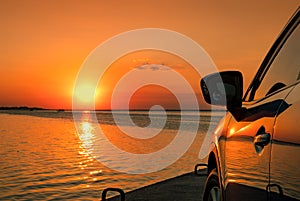 Blue compact SUV car parked on concrete road by the sea at sunset.