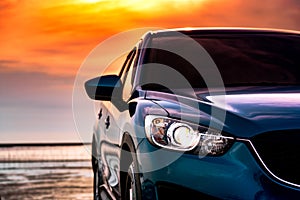 Blue compact SUV car with sport and modern design parked on the beach by the sea at sunset. Environmentally friendly technology.