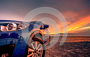 Blue compact SUV car with sport and modern design parked by beach at sunset. Hybrid and electric car technology. Car parking space