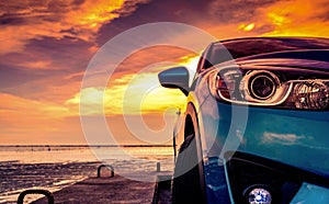 Blue compact SUV car with sport and modern design parked on concrete road by the sea beach at sunset. Front view of luxury car.