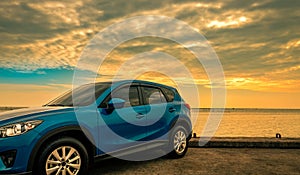 Blue compact SUV car with sport and modern design parked on concrete road by sea at sunrise. Environmentally friendly technology.