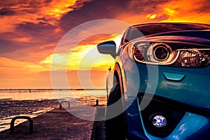 Blue compact SUV car with sport and modern design parked on concrete road by the sea at sunset. Environmentally friendly