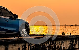 Blue compact SUV car with sport and modern design parked on concrete road by the sea at sunset. Environmentally friendly