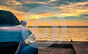 Blue compact SUV car with sport and modern design parked on concrete road by the sea at sunset in the evening. Hybrid and electric