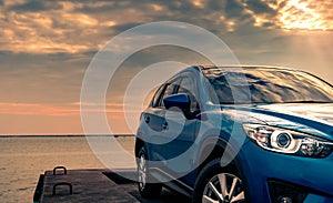 Blue compact SUV car with sport and modern design parked on concrete road by the sea at sunset in the evening. Hybrid and electric