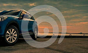 Blue compact SUV car with sport and modern design parked on concrete road by the sea at sunset in the evening. Hybrid and electric