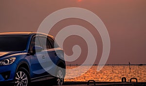 Blue compact SUV car with sport and modern design parked on concrete road by the sea at sunset in the evening. Hybrid and electric
