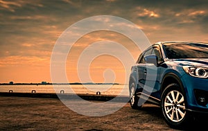 Blue compact SUV car with sport and modern design parked on concrete road by the sea at sunset in the evening. Hybrid and electric