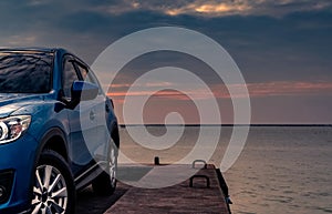 Blue compact SUV car with sport and modern design parked on concrete road by the sea at sunset in the evening. Hybrid and electric